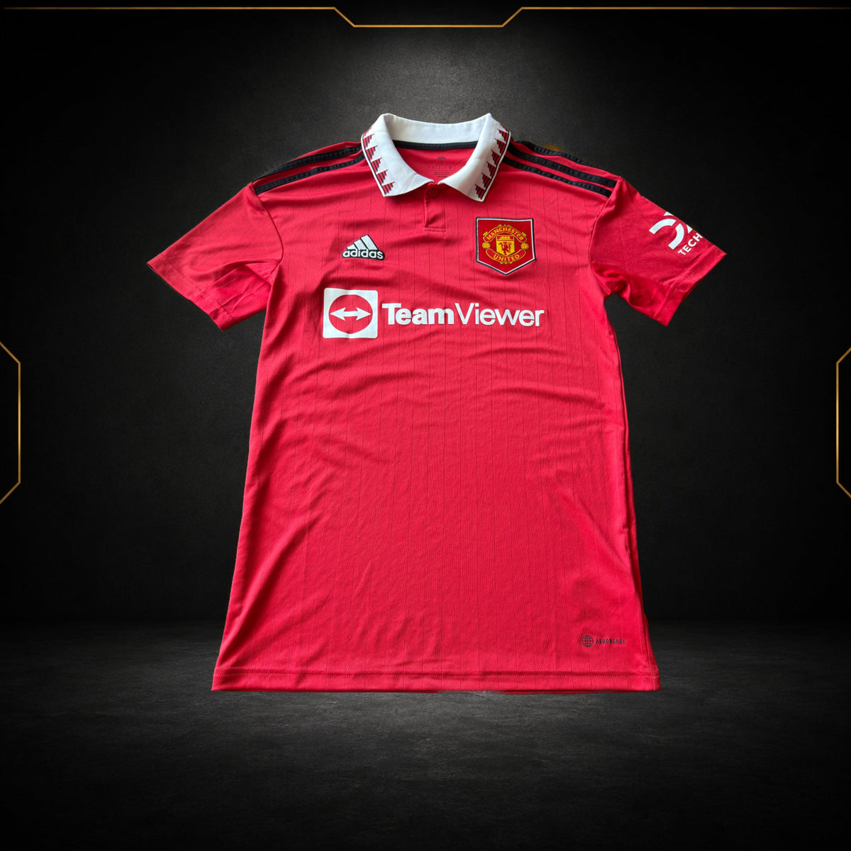 Maillot authentique Manchester United 2022/23 rouge photographié de face sur fond noir et doré par Maillots Market